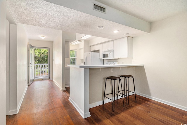 157 Egret Run Ln Unit 523, Pawleys Island, SC 29585 - kitchen with white appliances, a textured ceiling, dark wood-style floors, a kitchen breakfast bar, and a peninsula