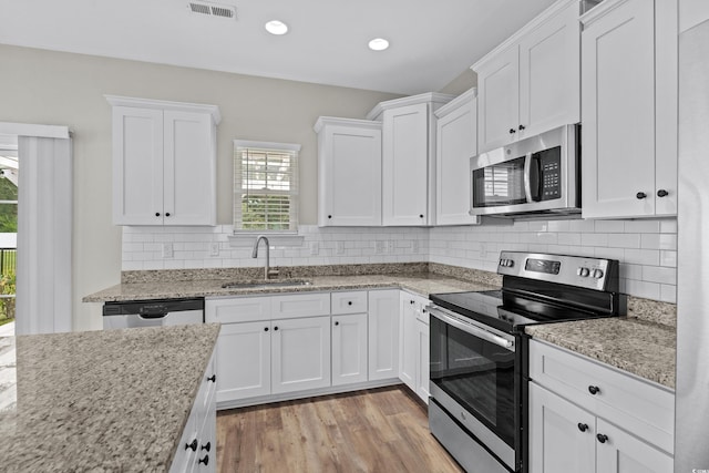 104 Browns Hollow Ct, Loris, SC 29569 - kitchen with appliances with stainless steel finishes, white cabinets, light wood-type flooring, tasteful backsplash, and light stone counters
