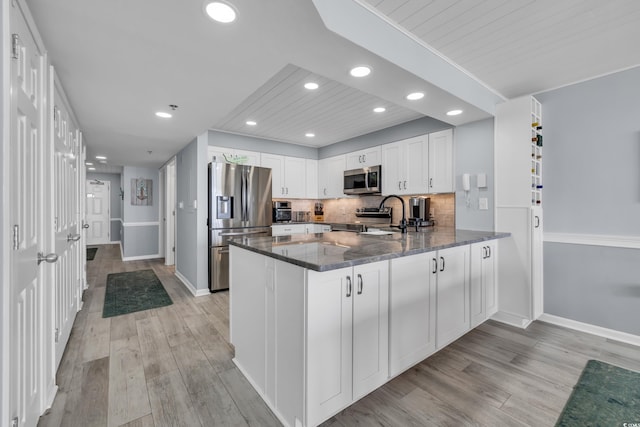 1625 S Ocean Blvd Unit 211, North Myrtle Beach, SC 29582 - kitchen featuring appliances with stainless steel finishes, dark stone counters, a peninsula, light wood-style flooring, and white cabinetry