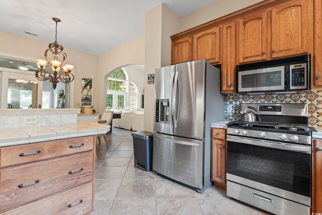 1501 Harbor Dr, North Myrtle Beach, SC 29582 - kitchen with stainless steel appliances, arched walkways, a chandelier, brown cabinetry, and tile countertops