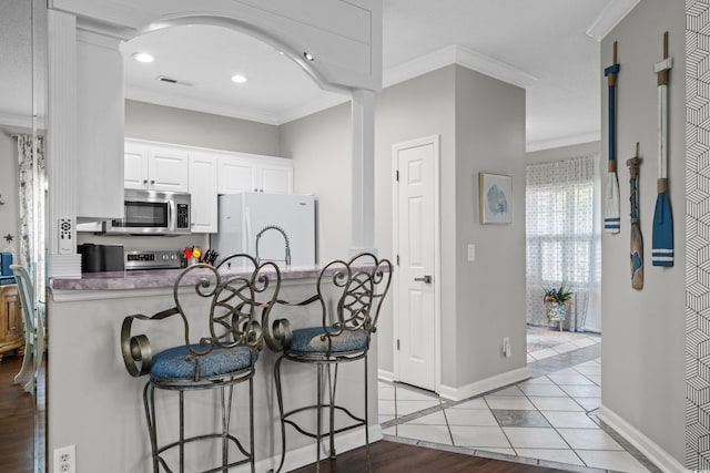 4648 Lightkeepers Way Unit 39A, Little River, SC 29566 - kitchen with appliances with stainless steel finishes, crown molding, a kitchen breakfast bar, white cabinetry, and recessed lighting