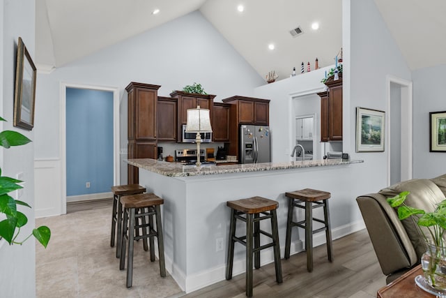 341 Bahama Dr, Murrells Inlet, SC 29576 - kitchen with stainless steel appliances, high vaulted ceiling, a breakfast bar area, light stone counters, and a sink