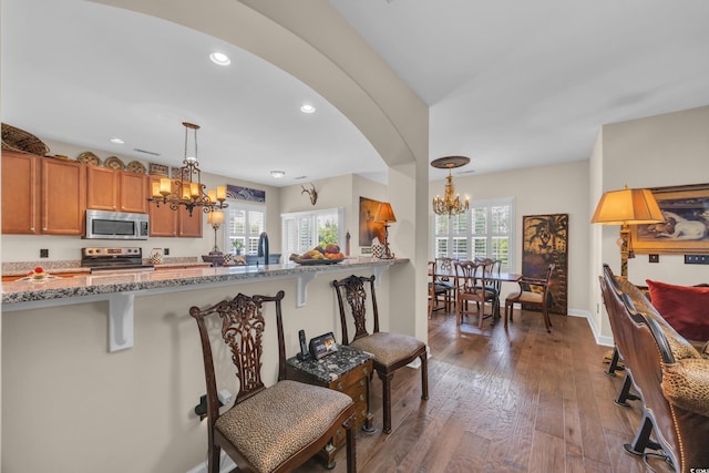 773 Wintercreeper Dr, Longs, SC 29568 - kitchen with a chandelier, stainless steel appliances, a breakfast bar area, brown cabinetry, and light stone counters