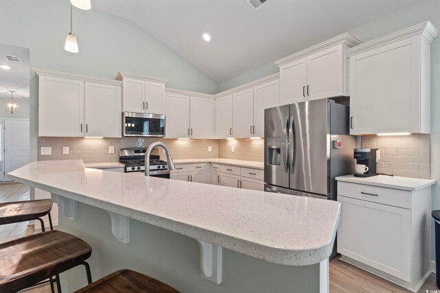 1178 Pyxie Moss Dr, Little River, SC 29566 - kitchen with appliances with stainless steel finishes, vaulted ceiling, a breakfast bar, white cabinetry, and tasteful backsplash