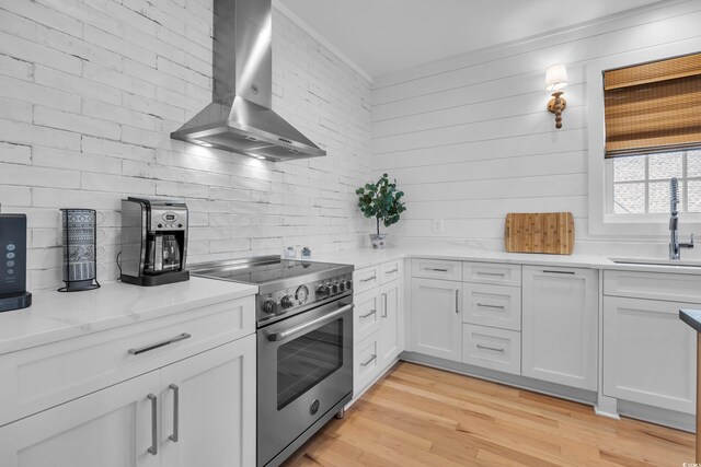 573 S Dunes Dr, Pawleys Island, SC 29585 - kitchen with high end stainless steel range oven, wall chimney range hood, white cabinets, and light wood-type flooring