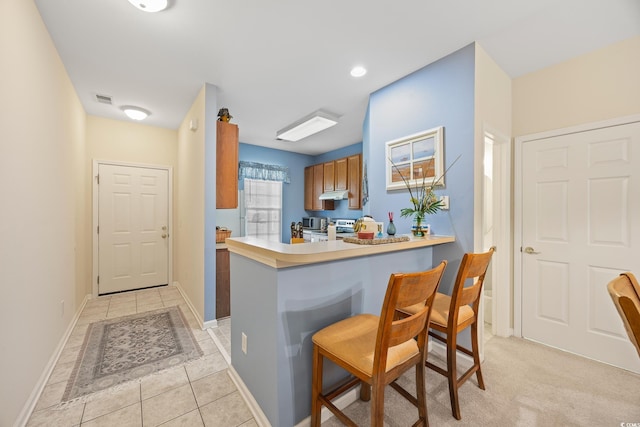 265 Connemara Dr Unit D, Myrtle Beach, SC 29579 - kitchen featuring under cabinet range hood, stainless steel stove, a kitchen breakfast bar, light tile patterned floors, and brown cabinetry