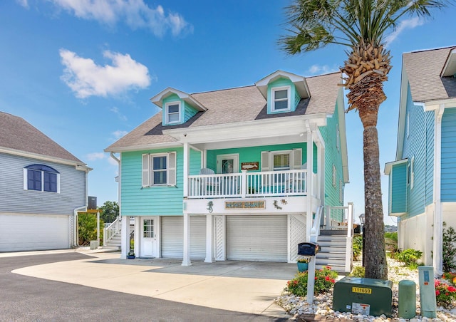 4534 Landing Rd, Little River, SC 29566 - raised beach house with stairway, a porch, a shingled roof, concrete driveway, and a garage
