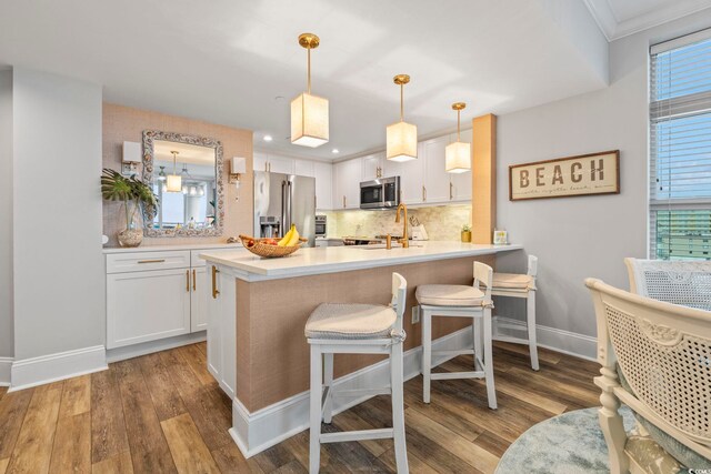603 S Ocean Blvd Unit 1504, North Myrtle Beach, SC 29582 - kitchen featuring stainless steel appliances, white cabinetry, tasteful backsplash, wood finished floors, and ornamental molding