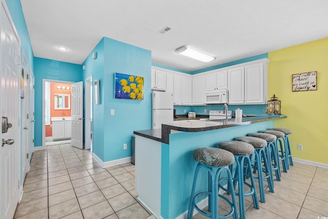 22 Ocean Blvd N, Surfside Beach, SC 29575 - kitchen featuring white appliances, a peninsula, light tile patterned floors, white cabinetry, and a breakfast bar