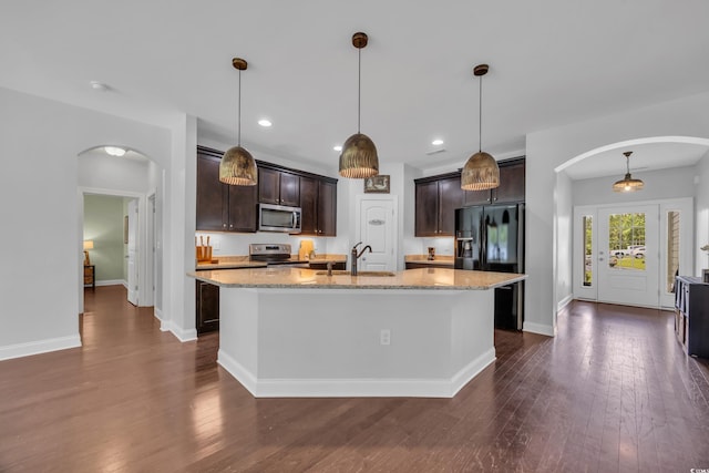 321 Sanctuary Ct, Myrtle Beach, SC 29588 - kitchen with stainless steel appliances, arched walkways, dark brown cabinetry, light stone counters, and an island with sink
