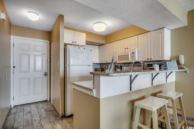 9400 Shore Dr Unit 617, Myrtle Beach, SC 29572 - kitchen with white appliances, a peninsula, a kitchen bar, decorative backsplash, and a textured ceiling
