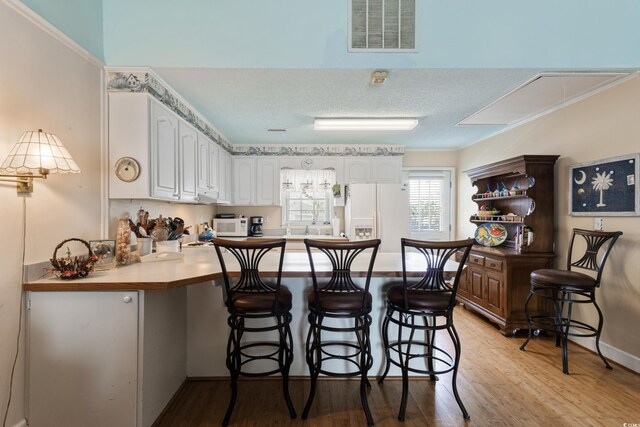 3307 Nixon St, North Myrtle Beach, SC 29582 - kitchen with white appliances, white cabinets, light wood finished floors, a peninsula, and a kitchen breakfast bar
