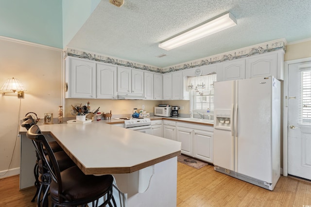 3307 Nixon St, North Myrtle Beach, SC 29582 - kitchen with white appliances, a peninsula, a textured ceiling, a kitchen bar, and light wood-type flooring