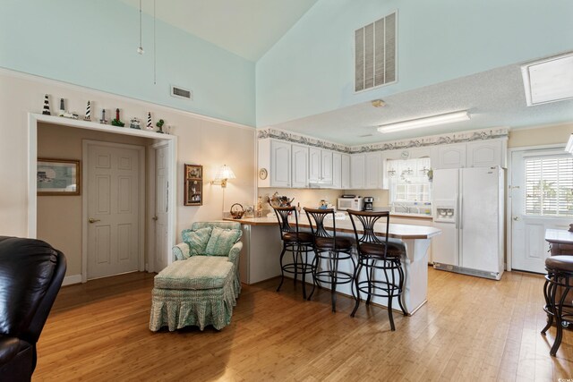 3307 Nixon St, North Myrtle Beach, SC 29582 - kitchen featuring white appliances, a peninsula, a high ceiling, a kitchen breakfast bar, and light wood-style flooring