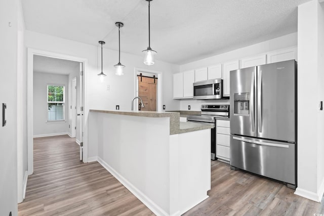 1331 Bermuda Ct, Surfside Beach, SC 29575 - kitchen featuring stainless steel appliances, a barn door, light wood-style floors, white cabinetry, and a peninsula