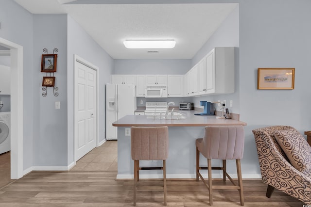 4520 Lighthouse Dr Unit 29B, Little River, SC 29566 - kitchen with white appliances, a peninsula, washer / clothes dryer, white cabinetry, and light wood-style floors