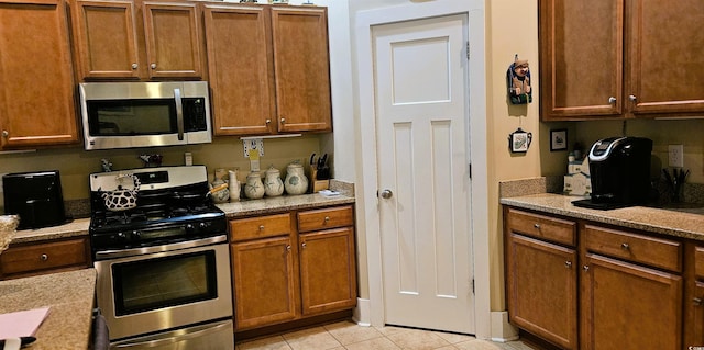 309 Outboard Dr, Murrells Inlet, SC 29576 - kitchen with appliances with stainless steel finishes, light tile patterned flooring, brown cabinetry, and light stone countertops