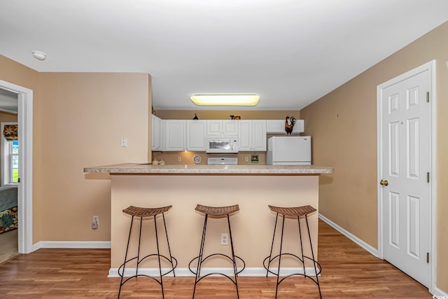 4366 Rivergate Ln Unit 306, Little River, SC 29566 - kitchen featuring white appliances, a kitchen breakfast bar, white cabinets, light wood-style floors, and light countertops