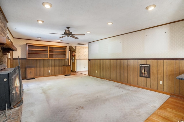 4920 Meadow St, Loris, SC 29569 - unfurnished living room featuring a wood stove, ornamental molding, ceiling fan, wallpapered walls, and a wainscoted wall