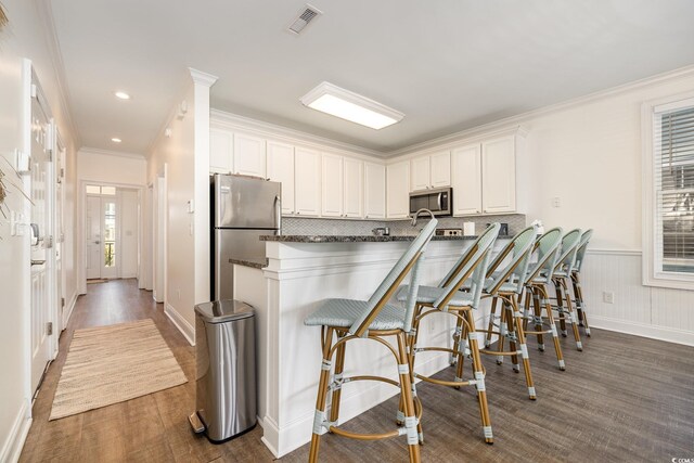 611 N Ocean Blvd, Surfside Beach, SC 29575 - kitchen with appliances with stainless steel finishes, a peninsula, crown molding, white cabinetry, and a kitchen bar