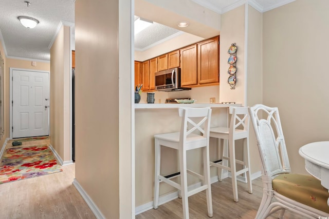 305 Hillside Dr N Unit 205, North Myrtle Beach, SC 29582 - kitchen with stainless steel microwave, ornamental molding, light wood-type flooring, a textured ceiling, and a breakfast bar area