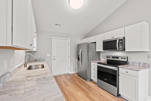 2965 Mount Olive Rd, Loris, SC 29569 - kitchen featuring appliances with stainless steel finishes, vaulted ceiling, white cabinetry, light wood finished floors, and a textured ceiling
