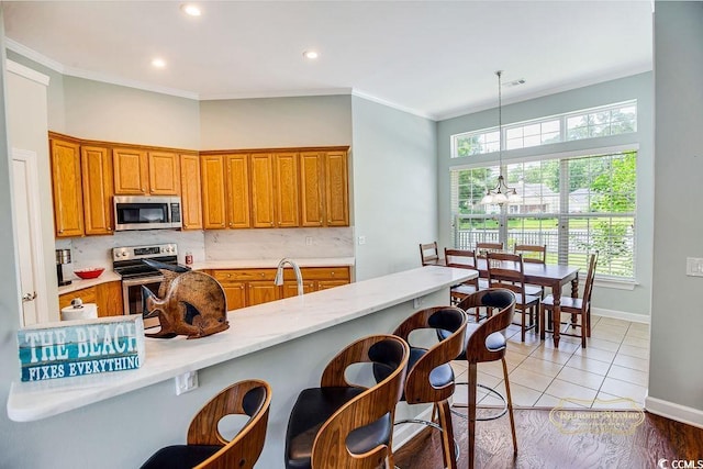 4499 Firethorne Dr, Murrells Inlet, SC 29576 - kitchen featuring appliances with stainless steel finishes, a chandelier, crown molding, brown cabinetry, and a breakfast bar