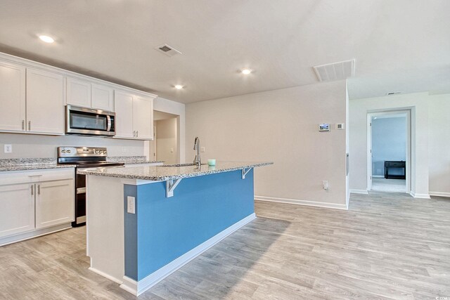 211 Seasons Trace Loop, Longs, SC 29568 - kitchen with appliances with stainless steel finishes, an island with sink, light wood finished floors, white cabinets, and light stone countertops