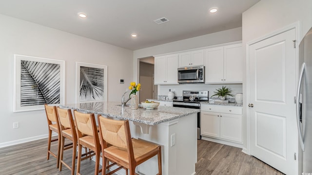 1407 Nokota Dr, Conway, SC 29526 - kitchen featuring appliances with stainless steel finishes, light wood finished floors, a kitchen island with sink, white cabinets, and light stone counters