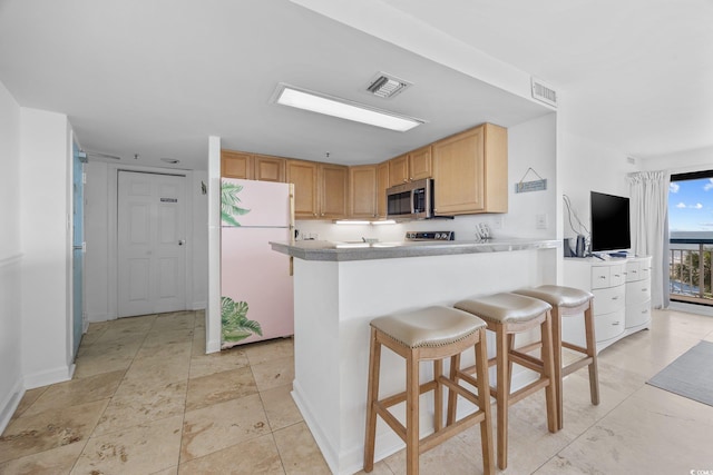 5511 N Ocean Blvd Unit 310, Myrtle Beach, SC 29577 - kitchen featuring freestanding refrigerator, stainless steel microwave, a kitchen bar, light brown cabinets, and a peninsula