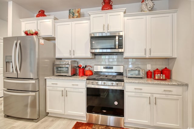 160 Juniata Loop, Little River, SC 29566 - kitchen with stainless steel appliances, white cabinets, light wood-style flooring, decorative backsplash, and light stone counters