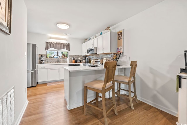 775 Plantation Dr Unit 53, Little River, SC 29566 - kitchen with stainless steel appliances, tasteful backsplash, a peninsula, light wood-style floors, and white cabinetry