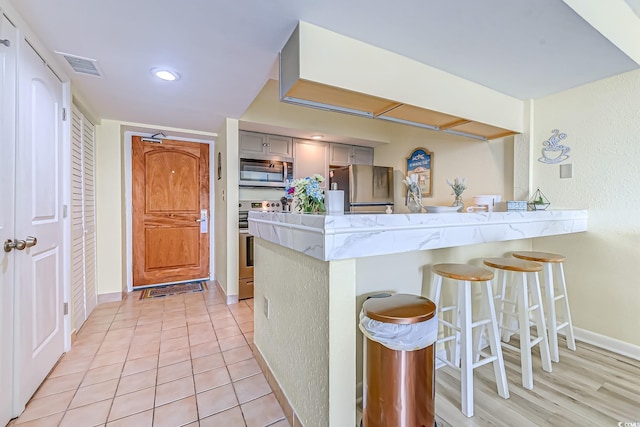 9550 Shore Dr Unit 225, Myrtle Beach, SC 29572 - kitchen featuring appliances with stainless steel finishes, a peninsula, gray cabinets, a kitchen breakfast bar, and light stone countertops