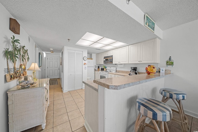 523 S Ocean Blvd Unit 305, North Myrtle Beach, SC 29582 - kitchen with white appliances, a kitchen bar, a textured ceiling, a peninsula, and white cabinets