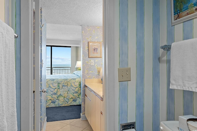 523 S Ocean Blvd Unit 305, North Myrtle Beach, SC 29582 - ensuite bathroom featuring wallpapered walls, a water view, vanity, a textured ceiling, and tile patterned flooring