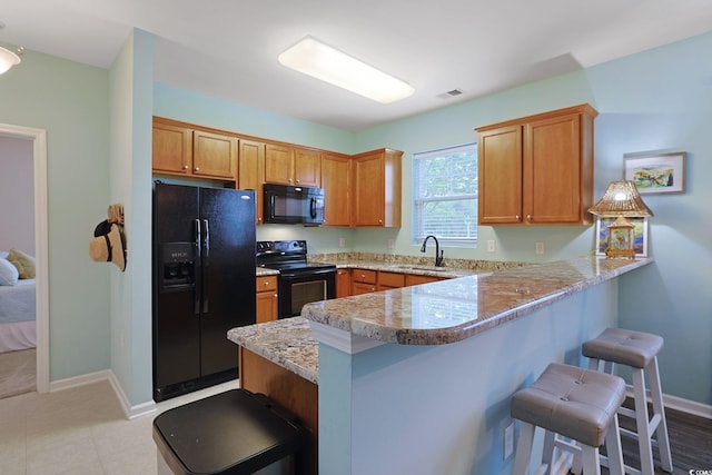 6253 Catalina Dr Unit 1711, North Myrtle Beach, SC 29582 - kitchen with black appliances, a kitchen bar, a peninsula, brown cabinets, and light stone counters