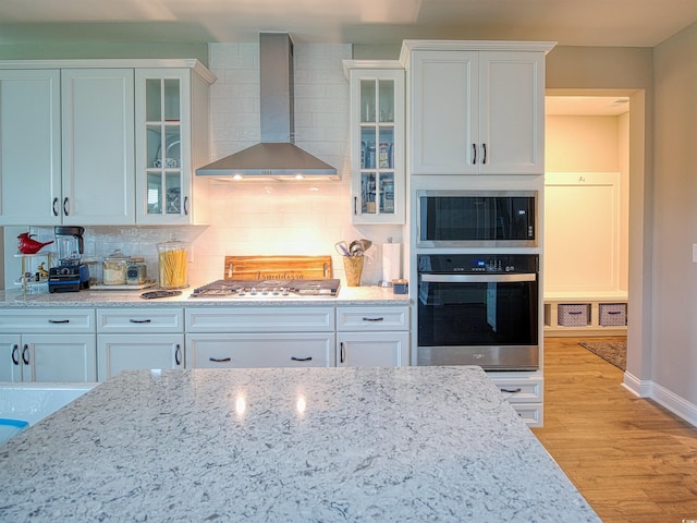 376 Mikita Dr, Surfside Beach, SC 29575 - kitchen featuring stainless steel appliances, wall chimney exhaust hood, tasteful backsplash, light stone counters, and light wood-style flooring