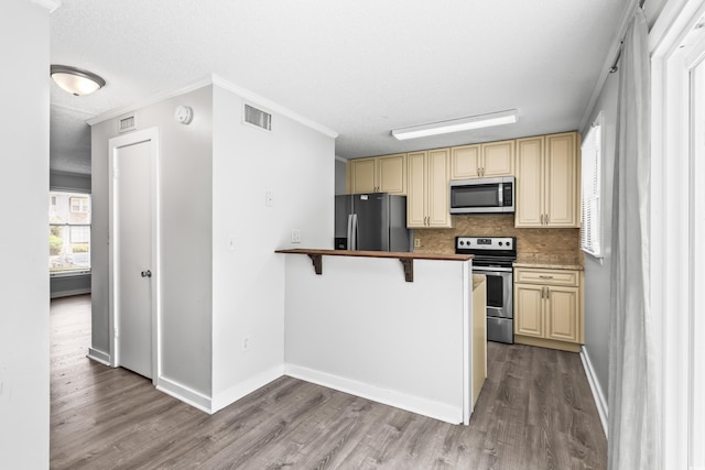 4115 Little River Rd Unit 1-E, Myrtle Beach, SC 29577 - kitchen featuring appliances with stainless steel finishes, cream cabinetry, wood finished floors, tasteful backsplash, and a peninsula