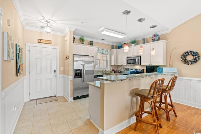 4865 Luster Leaf Cir Unit 402, Myrtle Beach, SC 29577 - kitchen with stainless steel appliances, wainscoting, stone counters, white cabinetry, and a peninsula