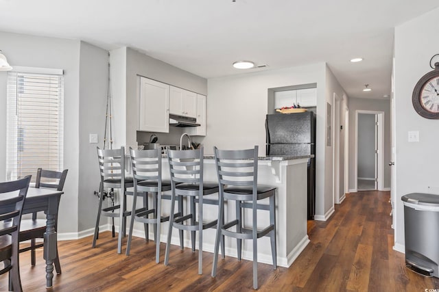 1100 Possum Trot Rd Unit F218, North Myrtle Beach, SC 29582 - kitchen featuring dark wood-style flooring, white cabinets, a breakfast bar area, under cabinet range hood, and a peninsula
