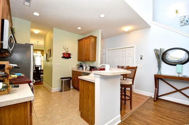 6172 Catalina Dr Unit 113, North Myrtle Beach, SC 29582 - kitchen with stainless steel microwave, a peninsula, a breakfast bar, brown cabinetry, and light countertops