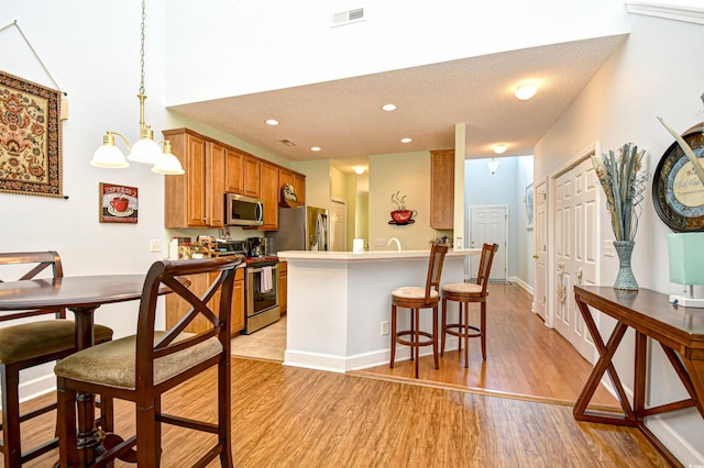 6172 Catalina Dr Unit 113, North Myrtle Beach, SC 29582 - kitchen featuring appliances with stainless steel finishes, light wood finished floors, brown cabinetry, a breakfast bar area, and a peninsula