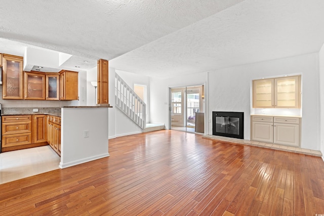 310 74th Ave N Unit 7, Myrtle Beach, SC 29572 - unfurnished living room with light wood-type flooring, a textured ceiling, stairway, and a glass covered fireplace