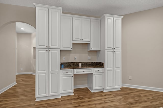 907 Tidewater Dr, North Myrtle Beach, SC 29582 - kitchen with arched walkways, built in study area, light wood-style flooring, white cabinets, and a textured ceiling