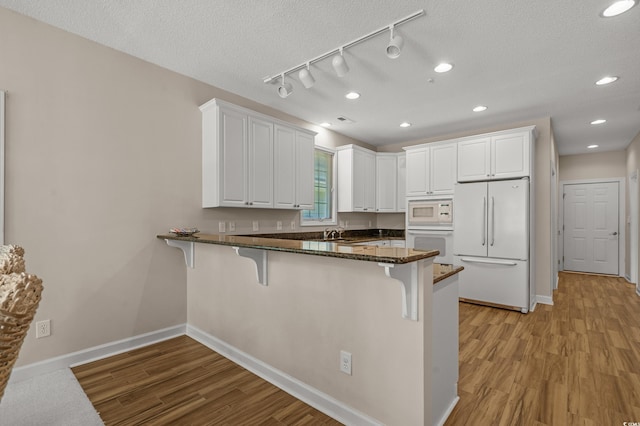 907 Tidewater Dr, North Myrtle Beach, SC 29582 - kitchen with white appliances, a peninsula, a breakfast bar area, white cabinets, and light wood-style flooring