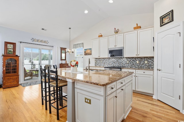 138 Copper Leaf Dr, Myrtle Beach, SC 29588 - kitchen featuring stainless steel microwave, vaulted ceiling, light wood-type flooring, decorative backsplash, and light stone counters