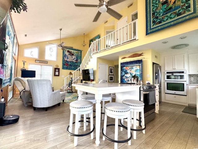 404 29th Ave N, North Myrtle Beach, SC 29582 - kitchen featuring a ceiling fan, appliances with stainless steel finishes, light wood-style floors, high vaulted ceiling, and a kitchen bar