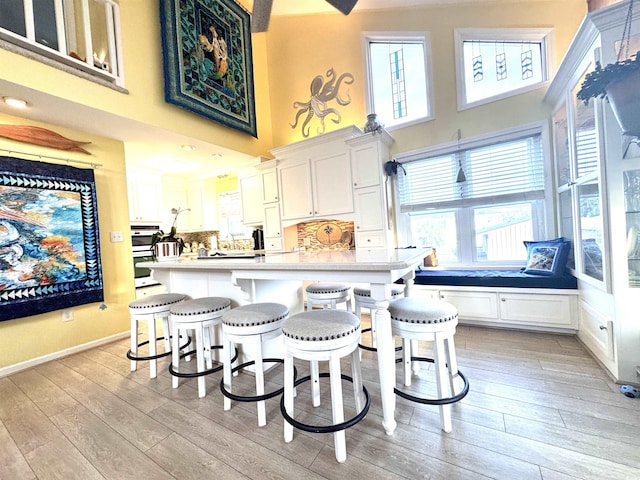 404 29th Ave N, North Myrtle Beach, SC 29582 - kitchen with a high ceiling, light wood finished floors, white cabinetry, a kitchen bar, and light countertops
