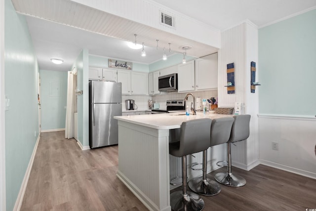 1011 S Ocean Blvd Unit 301, North Myrtle Beach, SC 29582 - kitchen featuring appliances with stainless steel finishes, a peninsula, backsplash, light wood-style floors, and crown molding