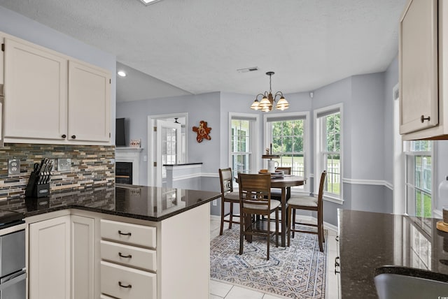 483 Oakmont Dr, Myrtle Beach, SC 29579 - kitchen featuring backsplash, a peninsula, a chandelier, light tile patterned floors, and dark stone countertops